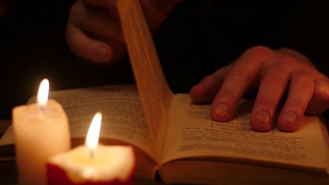 Man read book in darkness with candles. Leaf through by hands slow motion