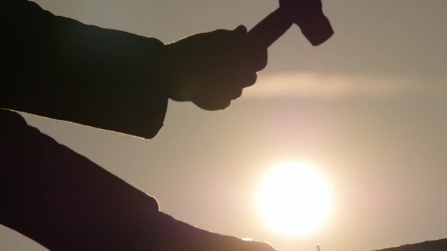 Mans hands silhouette starting hammer a nail with bright shining sun at evening