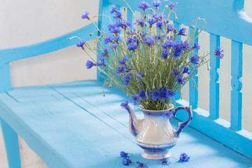 cornflowers in vase on blue bench