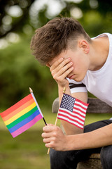 Depressed teenage boy with United States Flag and a Pride flag