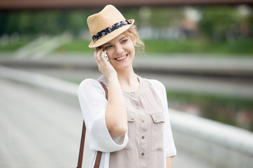 Portrait of smiling beautiful caucasian woman walking on the street and talking on smartphone. Female wearing casual clothing making call outdoors in summer. Attractive model using mobile phone