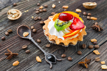 Rustic wooden  background with fruit tart and spices - cinnamon, anise, peanuts. Tasty dessert with strawberry, kiwi, orange, peach and whipped cream.
