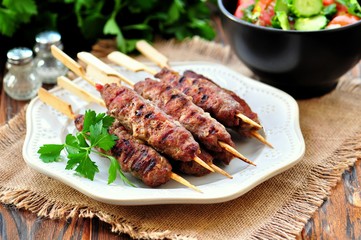 Homemade kebabs on skewers with a salad of tomato and cucumber.