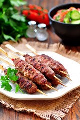 Homemade kebabs on skewers with a salad of tomato and cucumber.