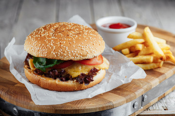 Hamburger with tomato and cheese, french fries and ketchup on a wooden board