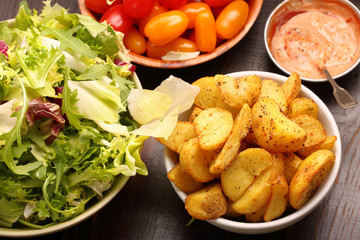 Roasted potatoes with dip and fresh salad on wooden table