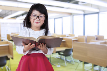 Fototapeta premium Little girl holds book in reading room