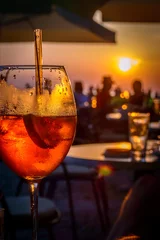 Muurstickers Een glas koude sinaasappelcocktail bij de zonsondergang op de tafel van een strandbar © t0m15
