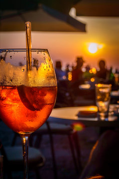 A glass of cold orange cocktail at the sunset on the table of a beach bar