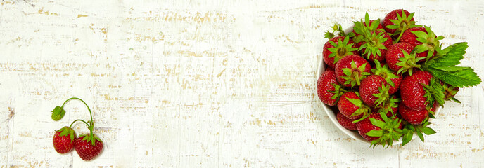 Ripe strawberries with leaves in white plate on wooden table. Top view. Copy space