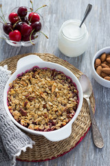 Homemade cherry crumble with oatmeal and almonds with fresh cherry and yogurt on a light wooden table