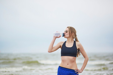 Young fitness running woman drinking water on beach