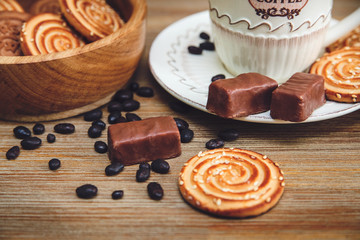 There are Cookies,Candy,Chocolate Peas,Poppy;Porcelain Saucer and Cap with Coffe,Tasty Sweet Food on the Wooden Background.Toned