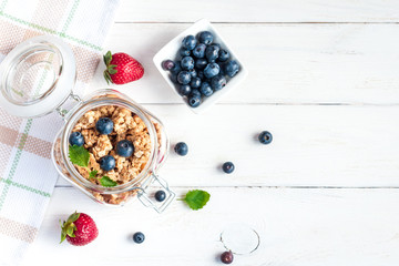 Naklejka na ściany i meble Healthy food. Muesli in the jar, blueberries and strawberries on white wooden background, top view, flat lay