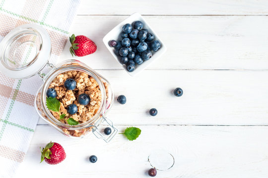 Healthy food. Muesli in the jar, blueberries and strawberries on white wooden background, top view, flat lay