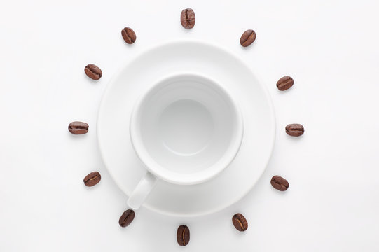 Empty coffee cup and coffee beans against white background forming clock dial viewed from top
