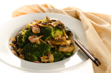 Broccoli sauteed with bacon, onion and mushrooms in white plate