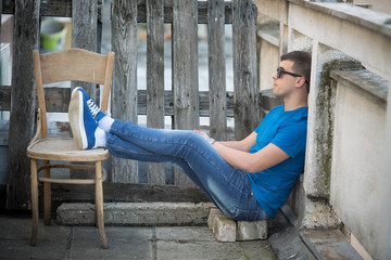 Young man chilling out on the floor. He is wearing a blue t-shirt and sunglasses.