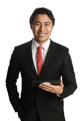 An attractive businessman under 30, wearing a black suit with red tie holding a digital tablet. White background.