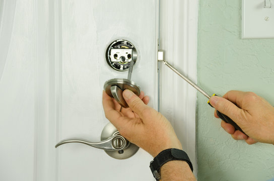Closeup of a professional locksmith is installing or repairing a new deadbolt lock on a house exterior door with the inside internal parts of the lock visible
