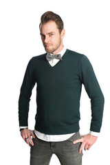 Trendy and fashionable man wearing a white shirt with a green pullover and bowtie, standing looking at camera in front of a white background.