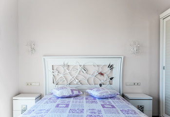 A bed in a bedroom. HeadBoard and purple cushions. Two bedside t