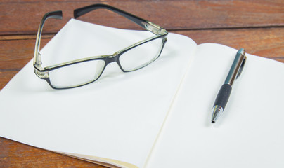 open notebook with pen and glasses on a wooden background