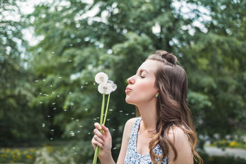 Young girl in a dress blowing dandelion in spring garden. Springtime. Spring allergy 
