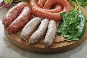 raw sausages for a barbecue with spinach leaves on wooden plate