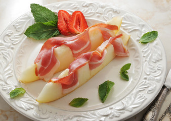 slices of melon wrapped in bacon with mint leaves and strawberry