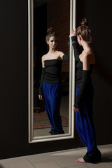 Pretty young model in fashion trousers and wool top near wall mirror