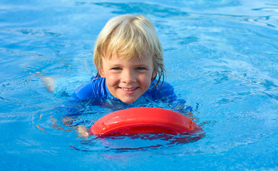 Happy  little boy has fun with floating board  in  swimming pool