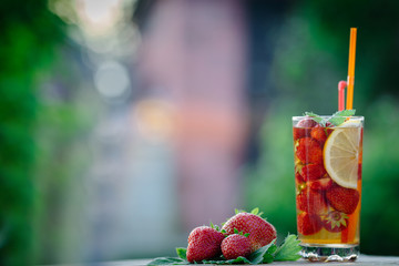 Glass of cold tea with mint,strawberry,lemon, on table, on green background,close up.