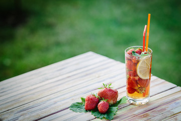Glass of cold tea with mint,strawberry,lemon, on table, on green background