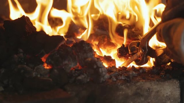 Blacksmith tongs pulls out of kiln red hot metal billet.