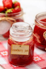 Strawberry jam in glass jars on wooden background.