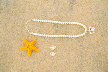 Fototapeta na wymiar Starfish and pearl necklace on the white sand at the beautiful beach on sunny day.