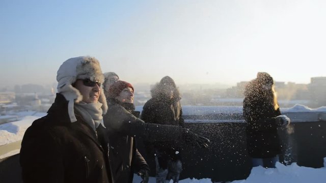 Young people playing snowball game on the roof of a high building