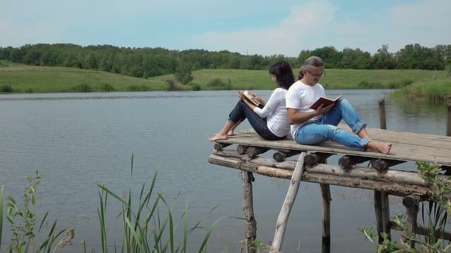 man and woman reading books on the board table near lake. 4K stock footage clip.
