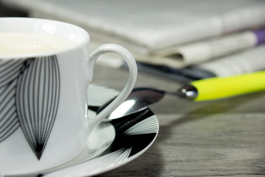 Eine Tasse Kaffee mit viel Milch und paar Zeitungem im Hintergrund