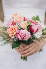 Beautiful bride in a wedding dress with bouquet and roses wreath posing in a green garden. Wedding day