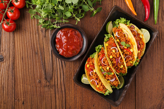 Tacos with meat and vegetables on wooden board