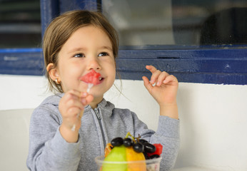 Happy little girl eating fruit salad using fork. Little girl eating healthy snack