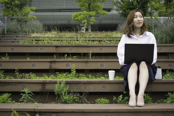 Japanese businesswoman using laptop computer on steps outside in Tokyo