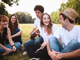 Fototapeta premium group of friends together in a park having fun and playing music with a guitar