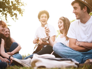 group of friends together in a park having fun and playing music with a guitar