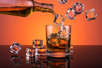 Whiskey pouring from bottle into glass full of ice - obrazy, fototapety, plakaty
