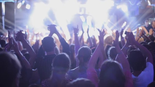 Large group of happy people enjoying rock concert, clapping with raised up hands, lights from the stage 1