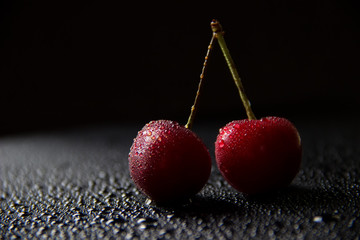 Pair of cherry over black reflective plane with water drops.