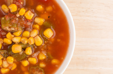 Corn okra and tomatoes soup in a white bowl on a table top close view.